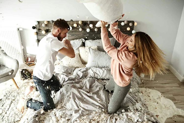 Affectionate couple and pillow fight at bedroom