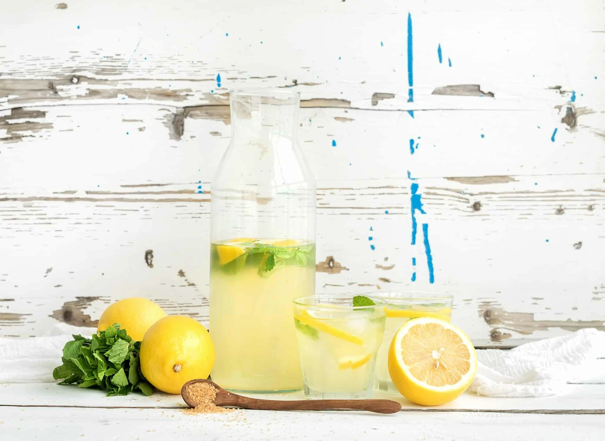 Fresh homemade lemonade with lemons and mint on white wooden background