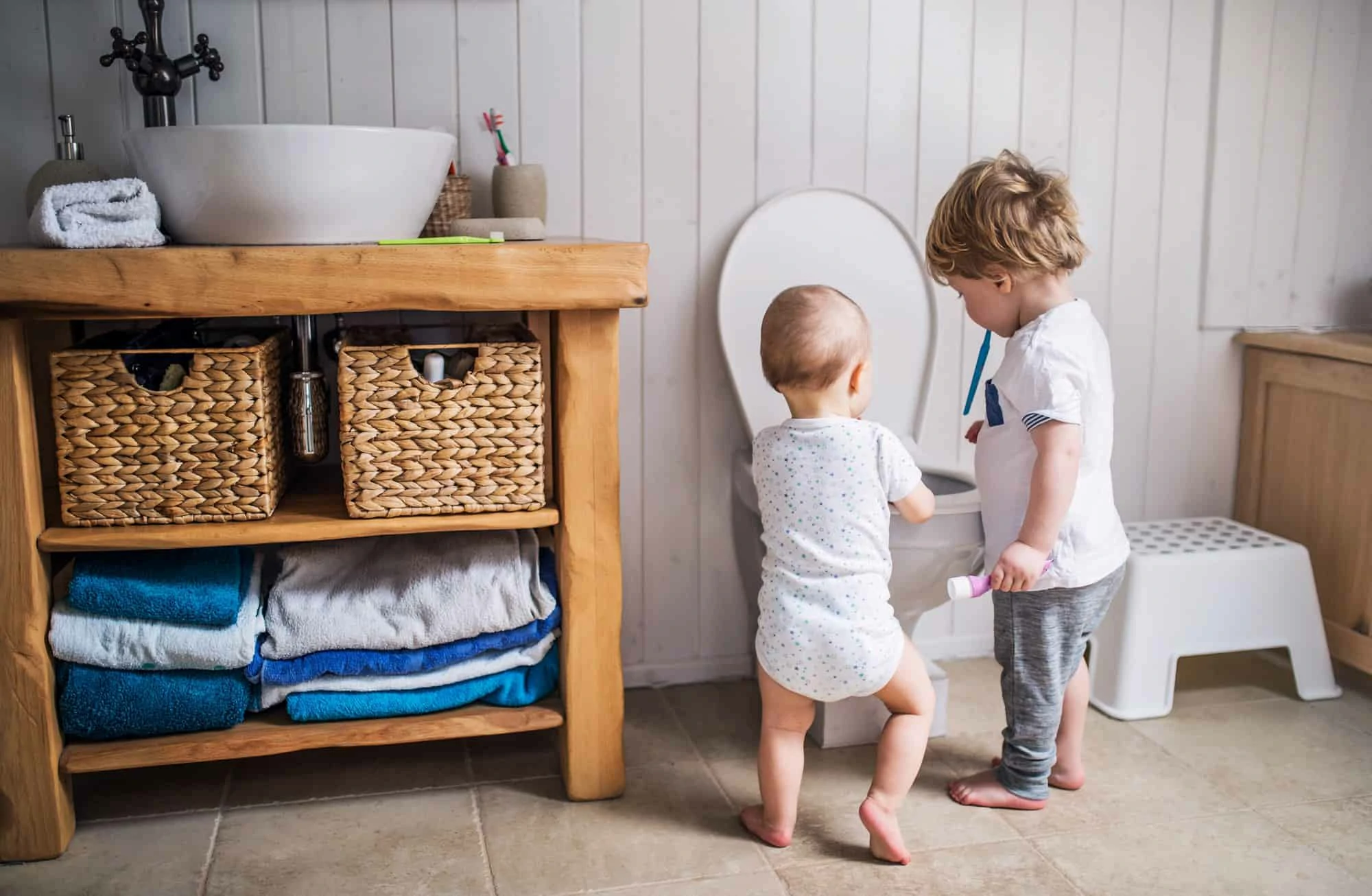 Two toddler children with toothbrush standing by the toilet in the bathroom at home.