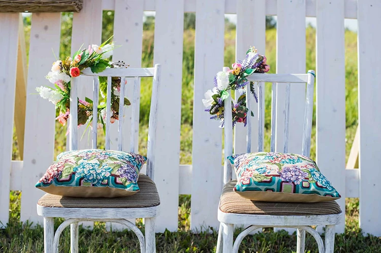 Two vintage white chairs, colorful velvet pillow and fence palisade on background decorated with