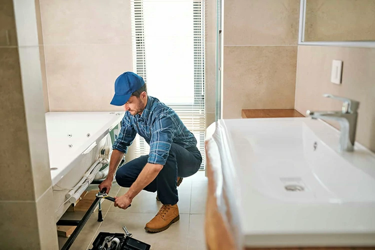 Young worker in uniform sitting on squats while fixing or fastening detail